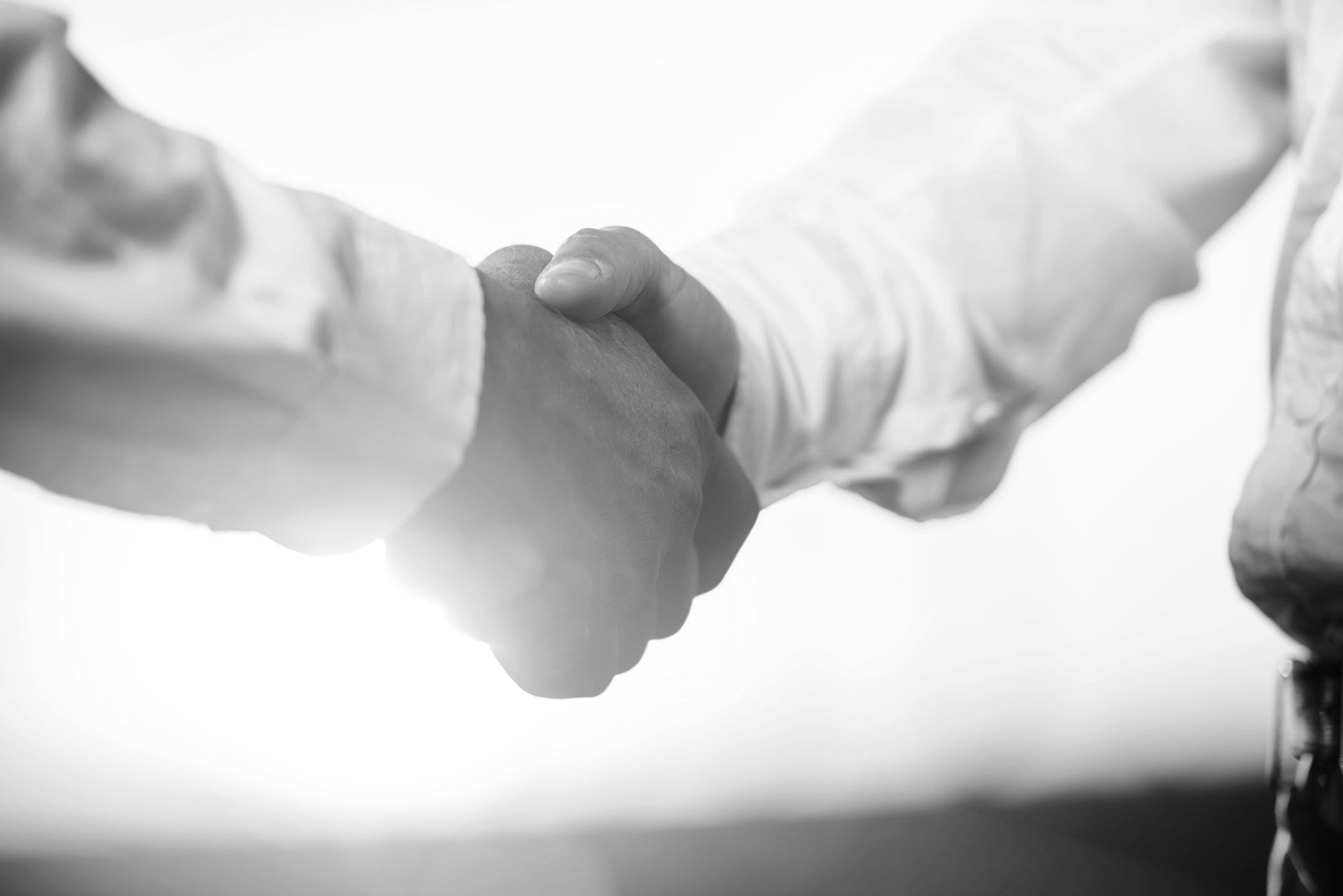 Two unrecognizable business people shaking hands at sunset.