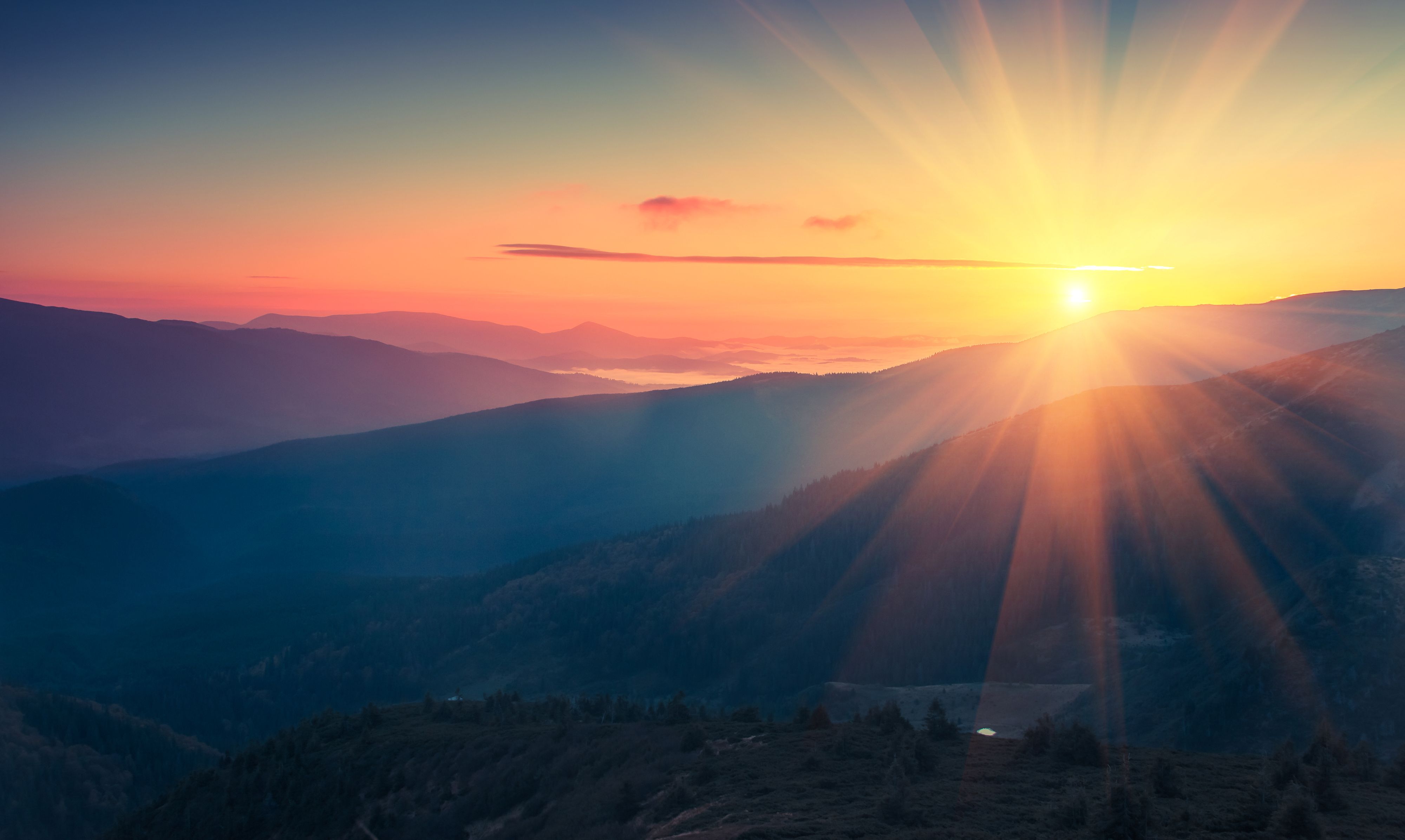 Mountainous landscape at sunrise with the sun shining its rays across the ground
