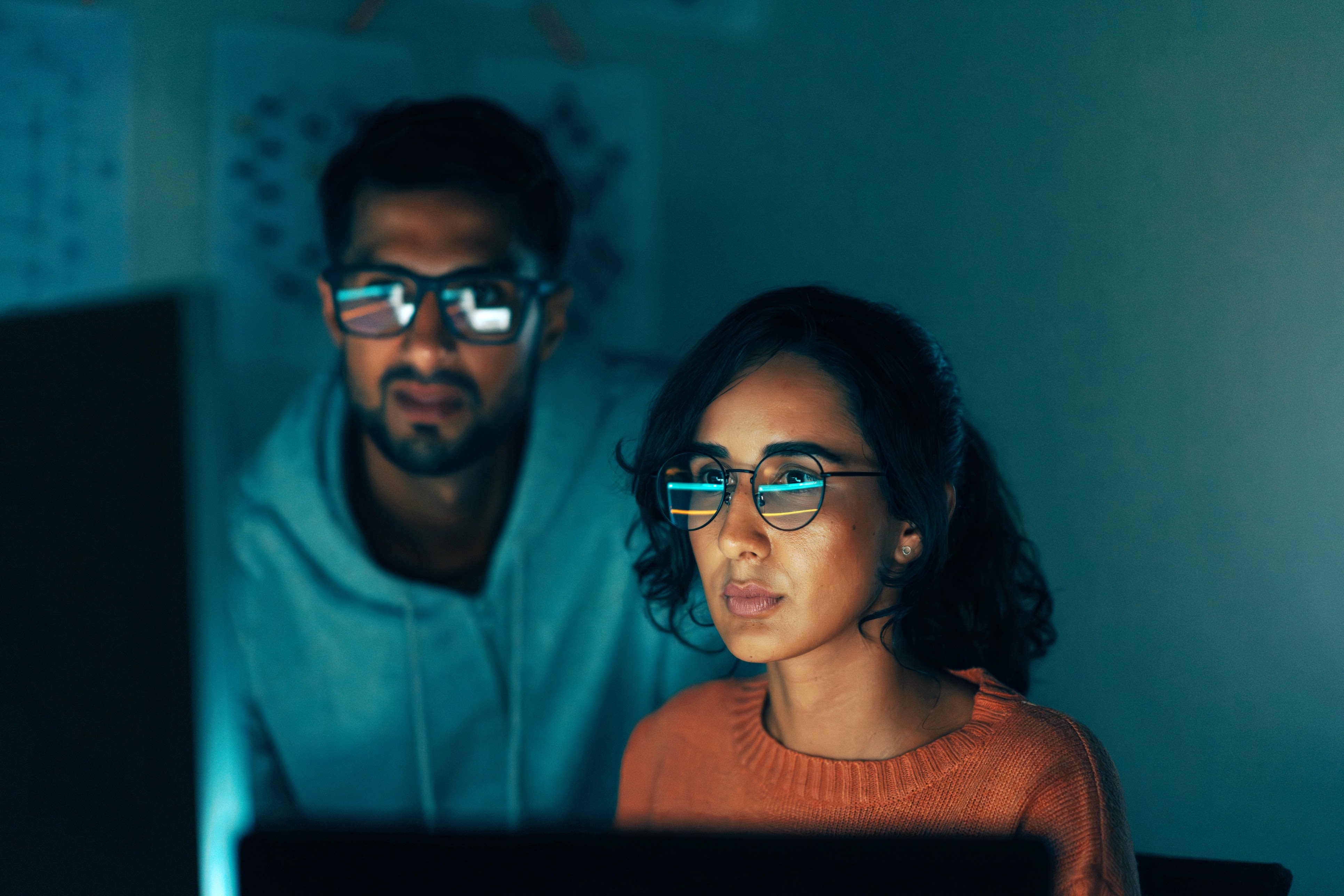 A woman and a man in front of a laptop, the monitor is reflected in their glasses.